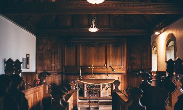 Interior of a wood panelled chapel. Altar at the far end with stalls facing the aisle in the foreground.